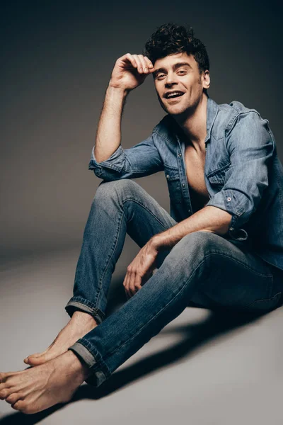 Sorrindo sexy homem posando em jeans roupas em cinza escuro — Fotografia de Stock