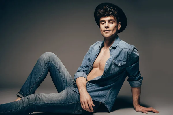 Schöner sexy Mann posiert in Jeans-Kleidung und Hut auf dunkelgrau — Stockfoto