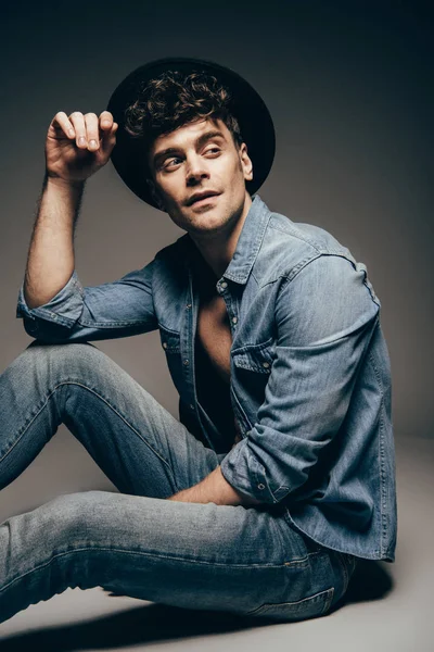 Stylische sexy Mann posiert in Jeans Kleidung und Hut auf dunkelgrau — Stockfoto