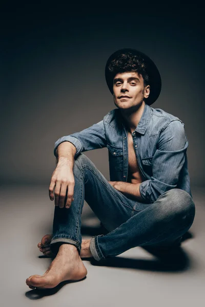 Schöner, stylischer Mann posiert in Jeanskleidung und Hut auf dunkelgrau — Stockfoto