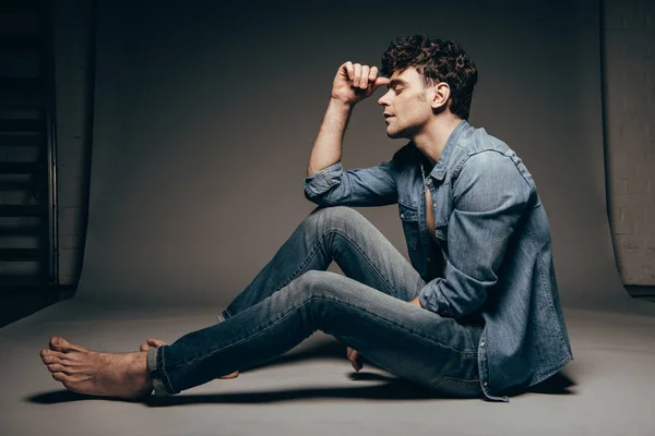 Descalzo reflexivo hombre posando en jeans ropa en gris oscuro - foto de stock