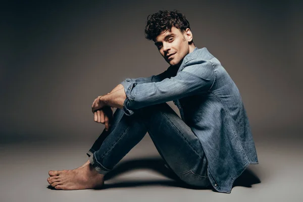 Sexy barefoot man sitting in jeans clothes on dark grey — Stock Photo