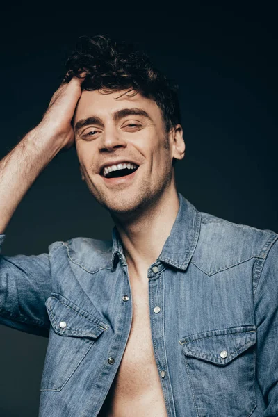 Hombre alegre guapo en camisa de mezclilla aislado en gris oscuro — Stock Photo