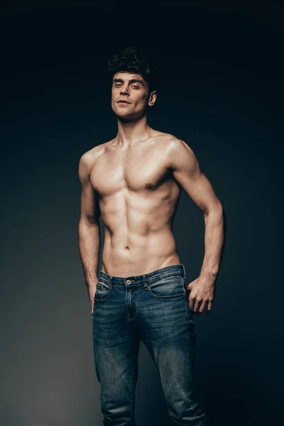 Sexy macho in jeans posing isolated on dark grey — Stock Photo