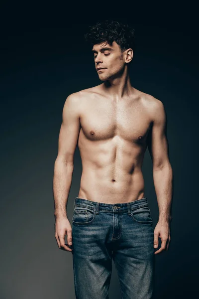 Sexy sin camisa musculoso hombre en jeans posando aislado en gris oscuro - foto de stock