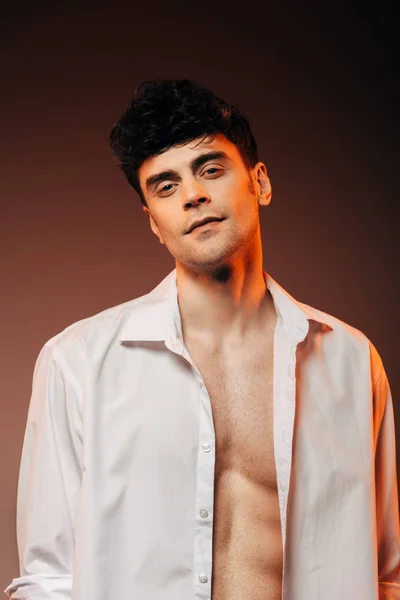 Модный сексуальный мужчина позирует в белой рубашке, изолированный на коричневый — стоковое фото