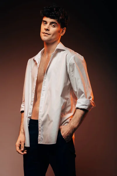 Сексуальний стильний чоловік позує в білій сорочці, ізольований на коричневому — стокове фото