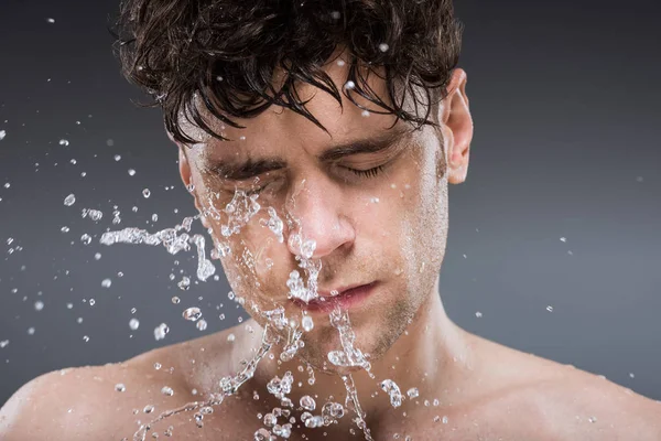 Красивий чоловік миє обличчя з водою вранці, ізольований на сірому — стокове фото