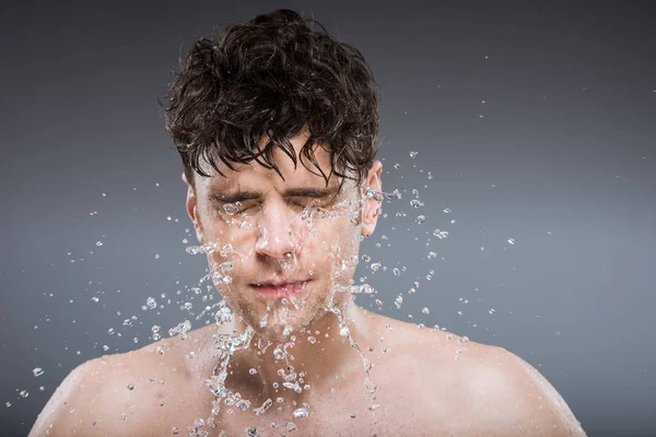 Schöner Mann wäscht Gesicht mit Wassertropfen, isoliert auf grau — Stockfoto