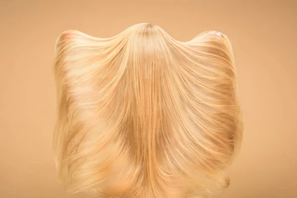 Rückansicht einer Frau, die mit ihren langen Haaren auf beigem Hintergrund spielt — Stockfoto