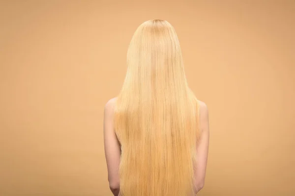 Visão traseira da mulher loira de cabelos longos em pé no fundo bege — Fotografia de Stock