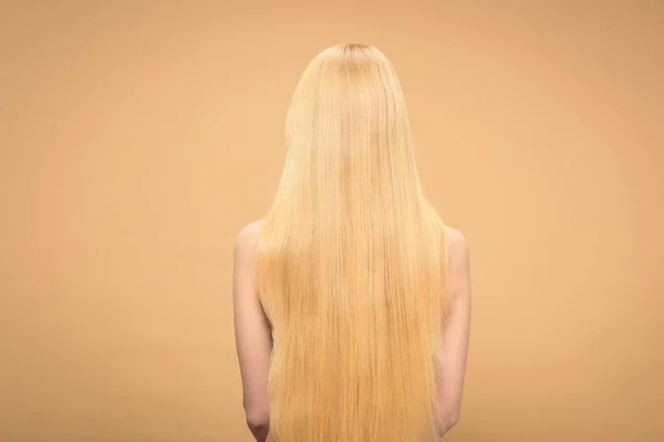 Back view of long-haired blonde woman standing on beige background — Stock Photo