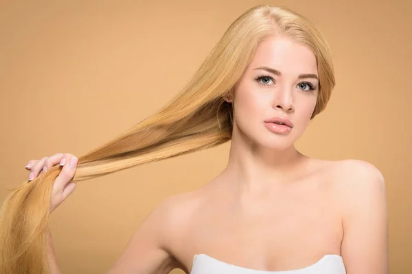 Menina bonita segurando longos cabelos lisos no fundo bege — Fotografia de Stock