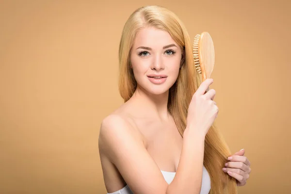 Vue de face de jolie femme blonde tenant une brosse à cheveux en bois — Photo de stock