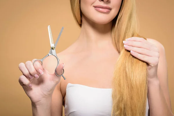 Cropped shot of smiling blonde girl with long hair holding scissors isolated on beige — Stock Photo