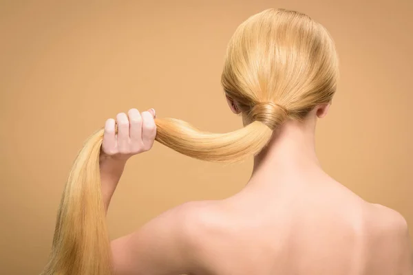 Vue arrière de la femme blonde nue tenant de longs cheveux raides isolés sur beige — Photo de stock