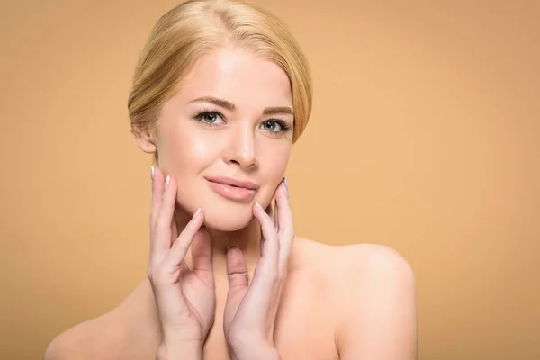 Attractive naked blonde girl touching face with hands and smiling at camera isolated on beige — Stock Photo