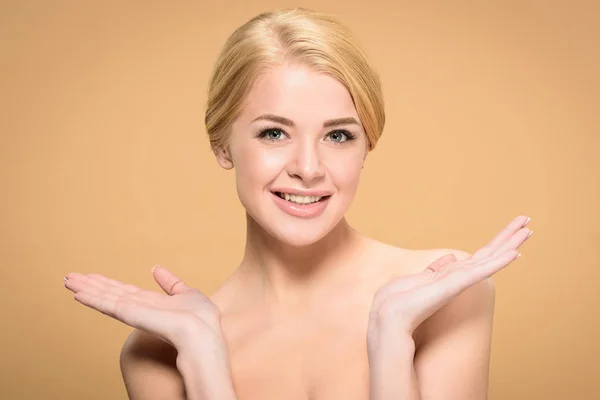 Beautiful naked woman gesturing with hands and smiling at camera isolated on beige — Stock Photo