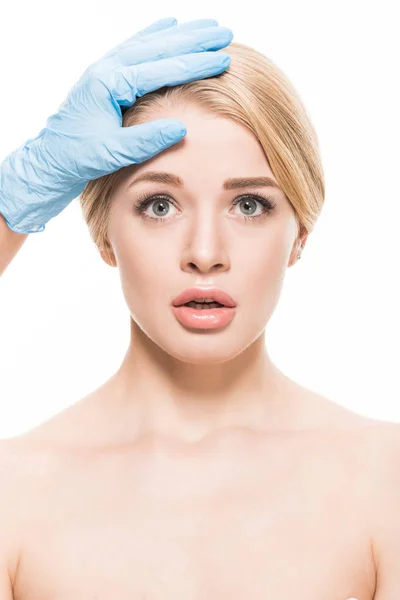 Tiro recortado de cosmetologista tocando a testa da jovem mulher assustada olhando para a câmera isolada no branco — Fotografia de Stock