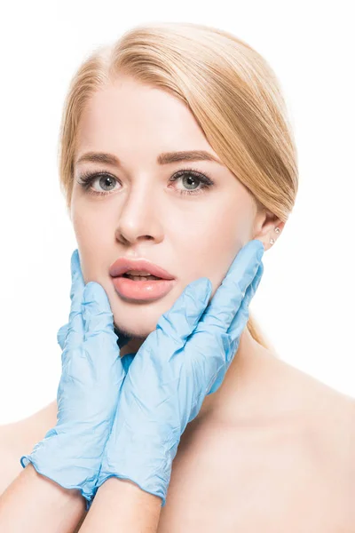 Abgeschnittene Aufnahme eines Kosmetikers in medizinischen Handschuhen, der das Gesicht einer jungen Frau berührt, die isoliert auf Weiß in die Kamera blickt — Stockfoto