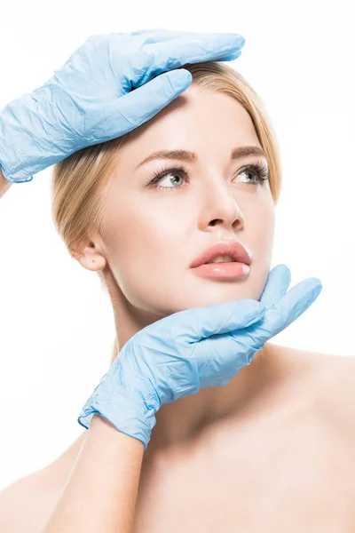 Cropped shot of cosmetologist in medical gloves touching face of beautiful woman isolated on white — Stock Photo