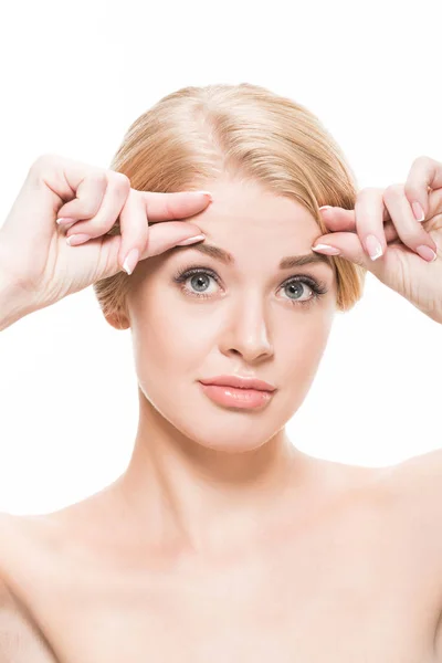 Naked young woman checking wrinkles on forehead and looking at camera isolated on white — Stock Photo