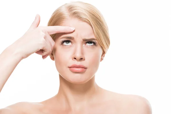 Unhappy young woman pointing at wrinkles on forehead and looking up isolated on white — Stock Photo