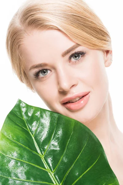 Bella donna bionda in possesso di foglia tropicale verde e sorridente alla fotocamera isolata su bianco — Foto stock