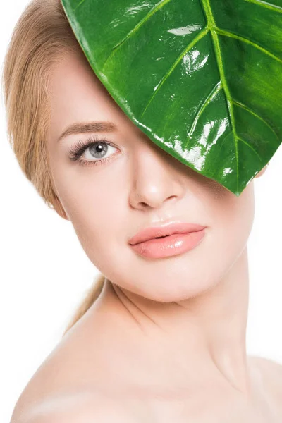 Menina nua atraente com folha verde perto do olho olhando para a câmera isolada no branco — Fotografia de Stock