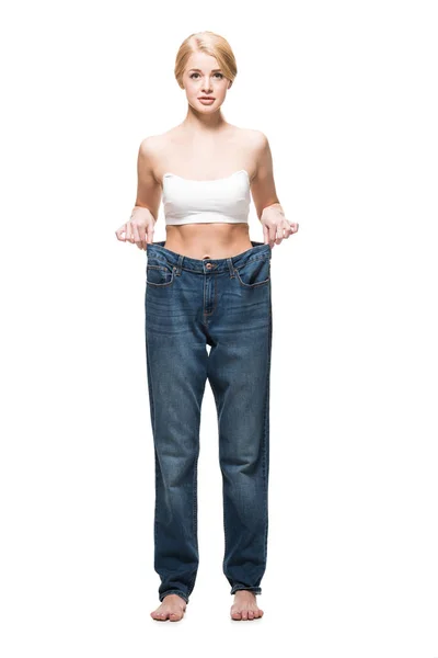 Full length view of barefoot slim girl wearing oversized jeans and looking at camera isolated on white — Stock Photo