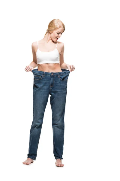 Vue pleine longueur de jeune femme surprise en jeans surdimensionnés regardant vers le bas isolé sur blanc — Photo de stock