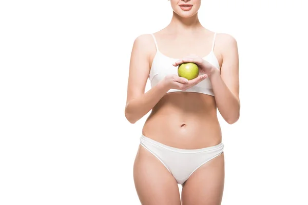 Обрізаний знімок тонкої молодої жінки в нижній білизні, що тримає свіже зелене яблуко ізольовано на білому — стокове фото