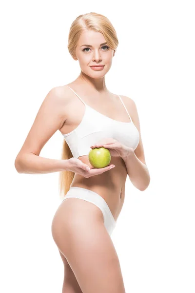Красива струнка жінка в нижній білизні тримає зелене яблуко і посміхається на камеру ізольовано на білому — стокове фото
