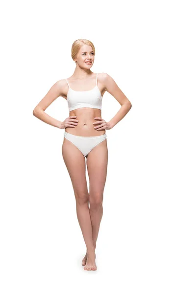 Full length view of smiling young woman in underwear standing with hands on waist and looking away isolated on white — Stock Photo