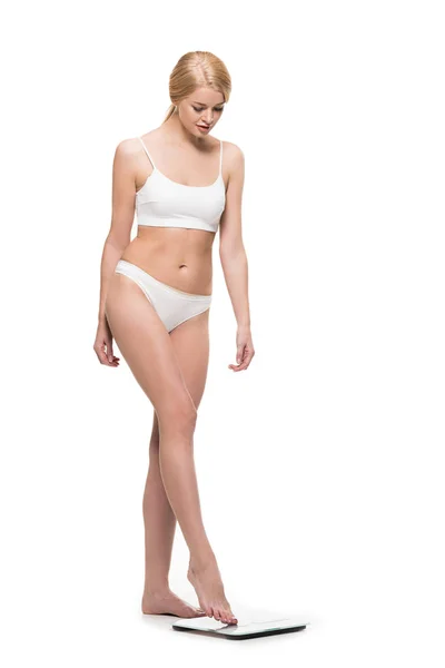 Schöne junge Frau in Unterwäsche tritt auf die Waage und schaut vereinzelt auf weiß herab — Stockfoto