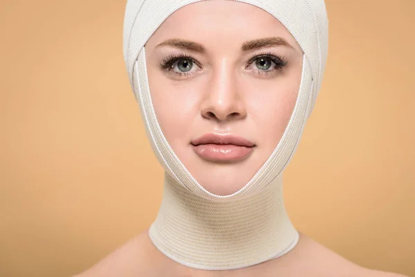 Jeune femme avec des bandages au-dessus de la tête regardant la caméra isolée sur beige, concept de chirurgie plastique — Photo de stock