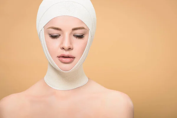Nackte junge Frau mit Binden über dem Kopf, die vereinzelt auf beige herabblickt — Stockfoto