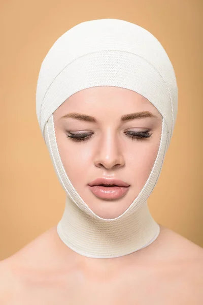 Mujer joven desnuda con vendajes sobre la cabeza mirando hacia abajo aislado en beige - foto de stock