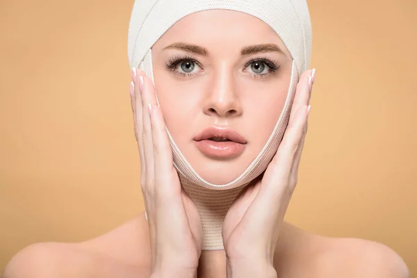 Jeune femme avec des bandages sur la tête touchant le visage et regardant la caméra isolée sur beige — Photo de stock