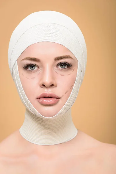 Jeune femme avec des bandages sur la tête et des lignes sur le visage regardant la caméra isolée sur beige — Photo de stock