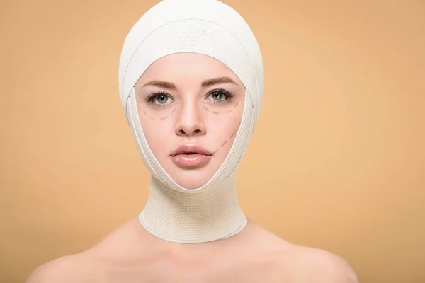 Mujer joven con vendajes sobre la cabeza y marcas en la cara mirando a la cámara aislada en beige - foto de stock