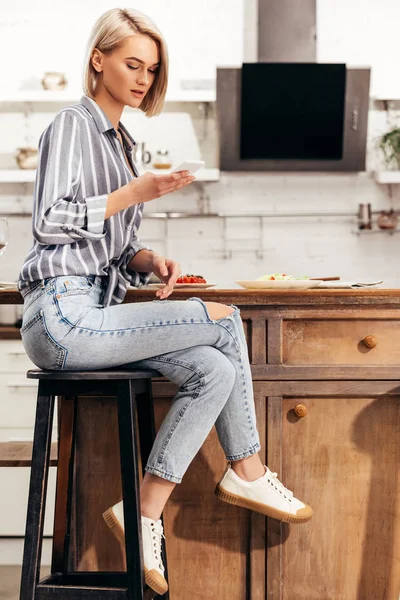 Atractiva mujer usando teléfono inteligente y sentado en la silla - foto de stock