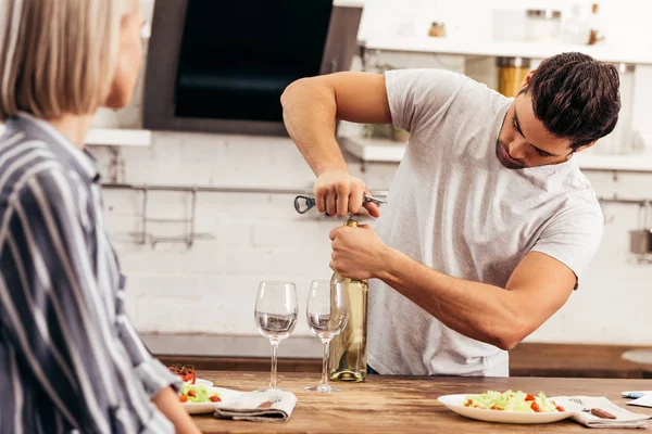 Guapo novio apertura vino botella cerca atractivo novia - foto de stock