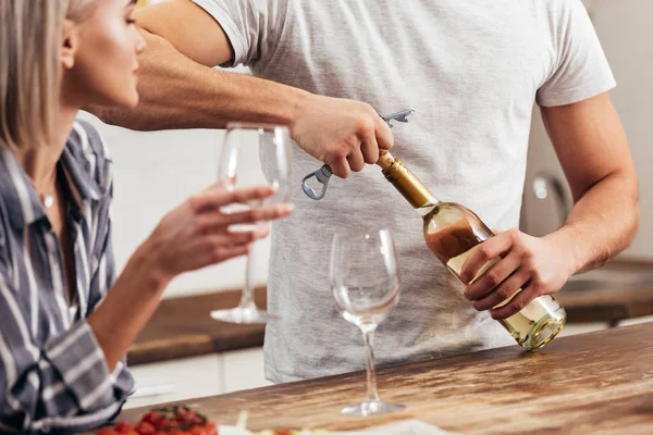 Vue recadrée de petit ami et ouverture bouteille de vin près de petite amie — Photo de stock