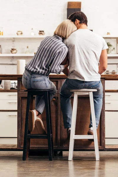 Vista trasera de novio y novia sentados en sillas en la cocina - foto de stock