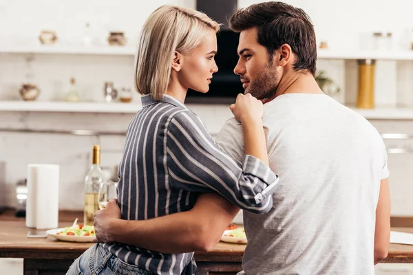 Schönes junges Paar schaut einander an und umarmt sich in der Küche — Stockfoto