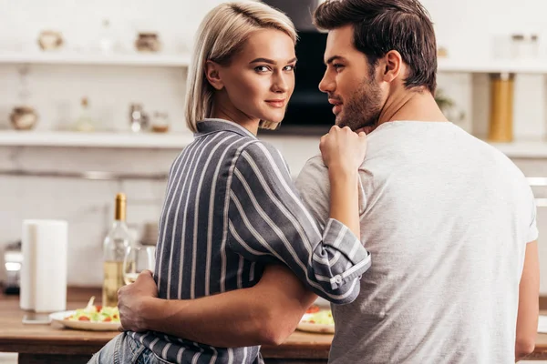 Schönes junges Paar, das sich in der Küche umarmt und in die Kamera schaut — Stockfoto