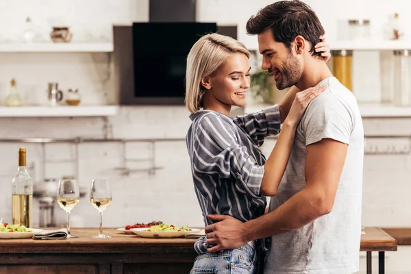 Красивый парень и привлекательная девушка улыбаются и обнимаются на кухне — стоковое фото