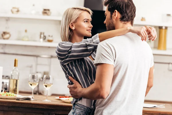 Novio guapo y novia atractiva abrazándose en la cocina - foto de stock