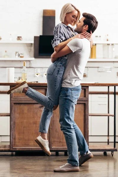 Novio guapo y novia atractiva abrazo y de pie en la cocina - foto de stock
